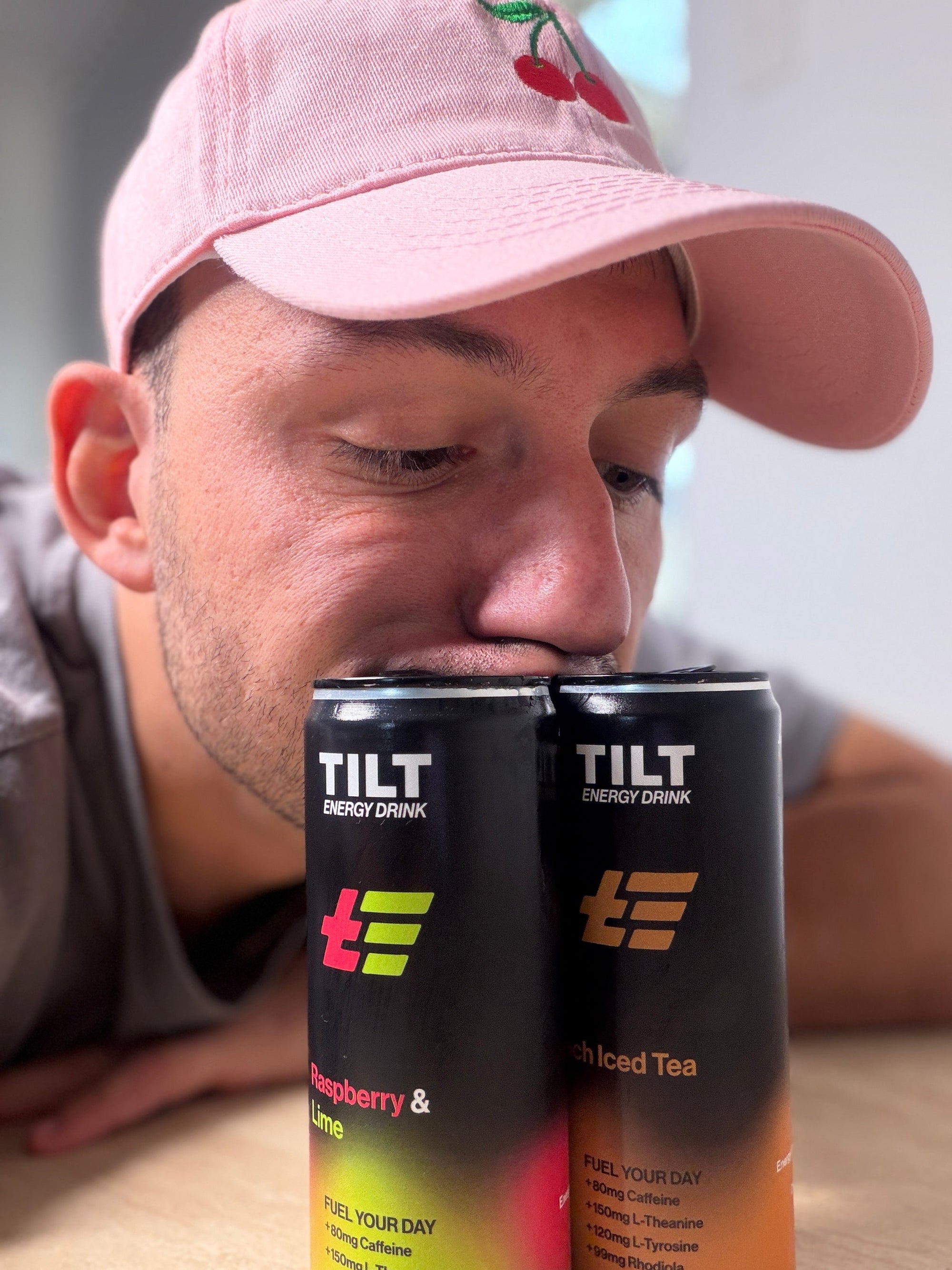 Man wearing a pink cap with two Australian Made TILT energy drink cans - Raspberry and Lime and Peach Iced Tea infront of him.