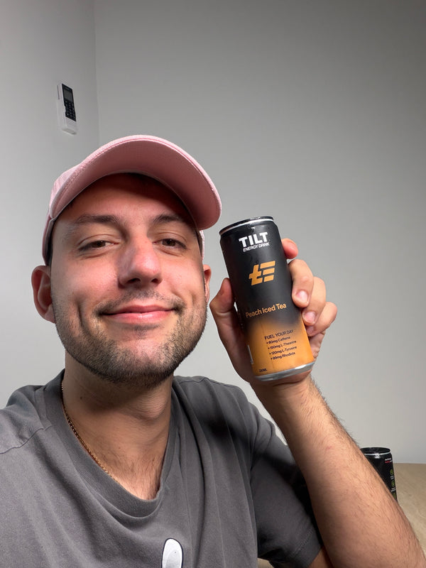 Holding an Australian Made Tilt Peach Iced Tea Energy Drink